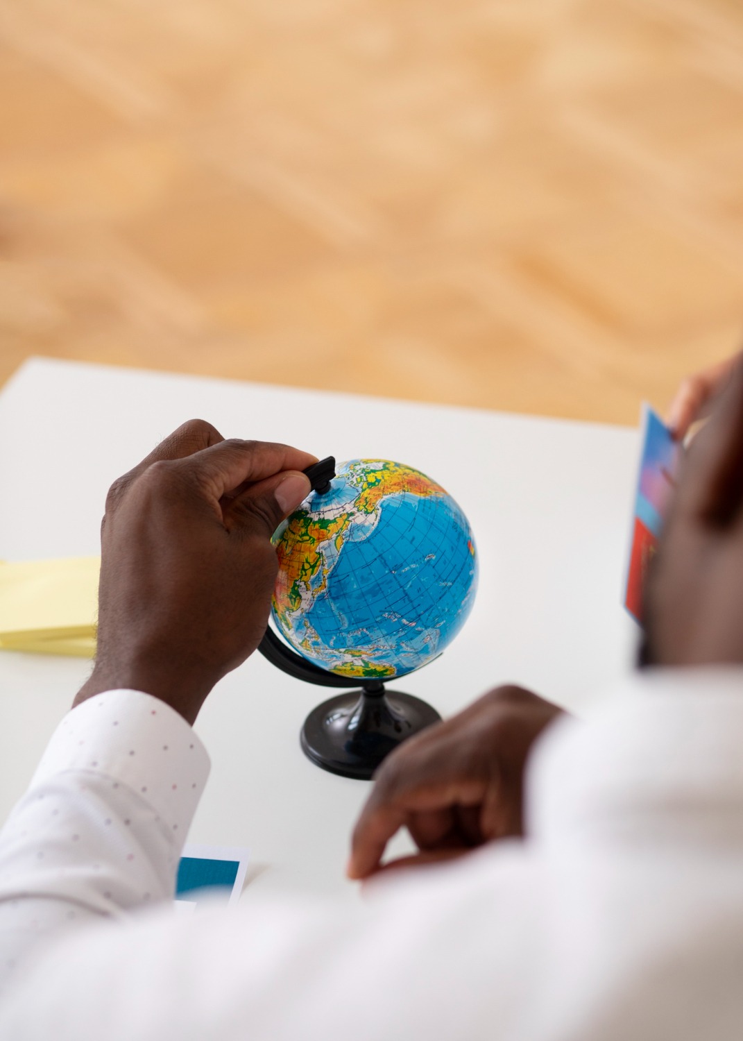 A hand holding a small globe at a desk